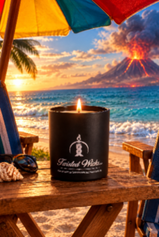Lit Eruption 7oz artisan candle in a matte black glass tumbler with white Twisted Wicks logo, on a beach table under an umbrella with a volcano erupting across the water at sunset