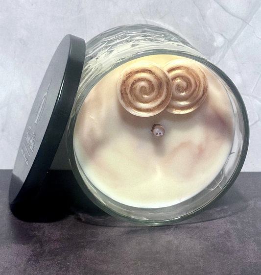 Sticky Situation 12oz artisan candle lying on its side, light beige wax topped with two cinnamon roll wax embeds and dusted with bronze mica