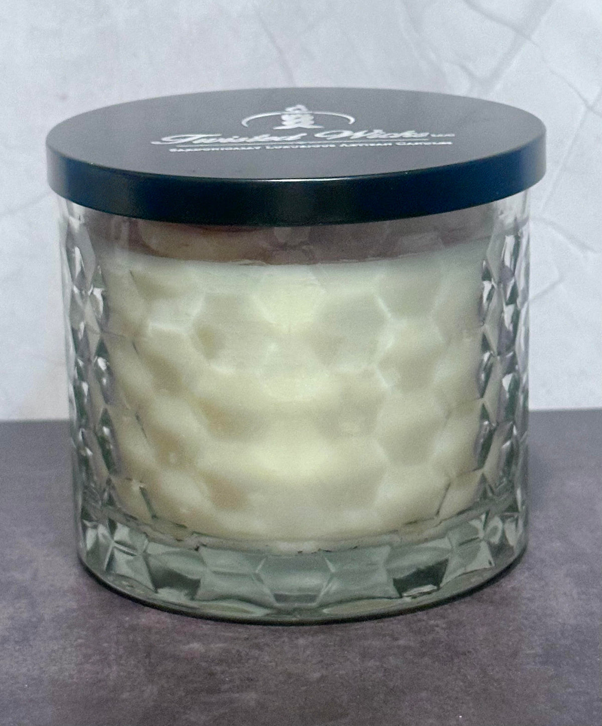 Sticky Situation 12oz artisan candle in a Hexagon patterned glass jar and a black lid featuring the 'Twisted Wicks' brand logo, set against a neutral gray background.